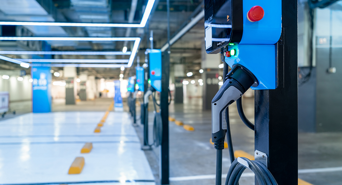 Electric car charging station for charge EV battery. Plug for vehicle with electric engine. EV charger. Clean energy. Charging point at car parking lot. Green power. Future transport technology.